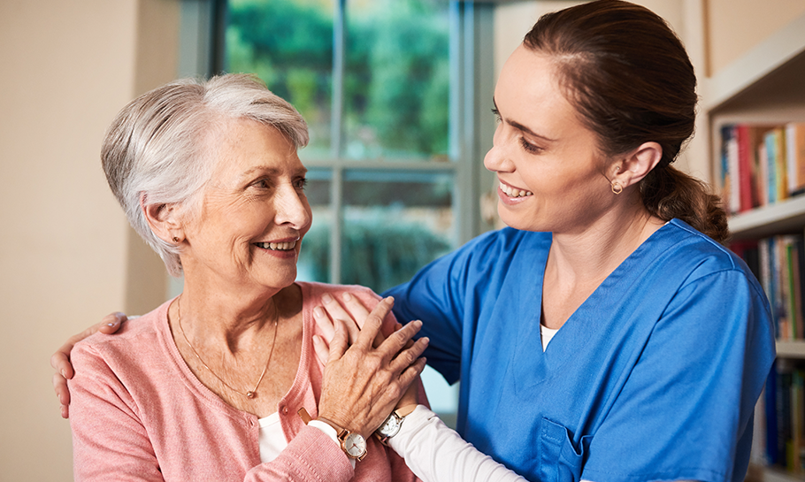 Senior woman and a nurse in scrubs smiling at each other