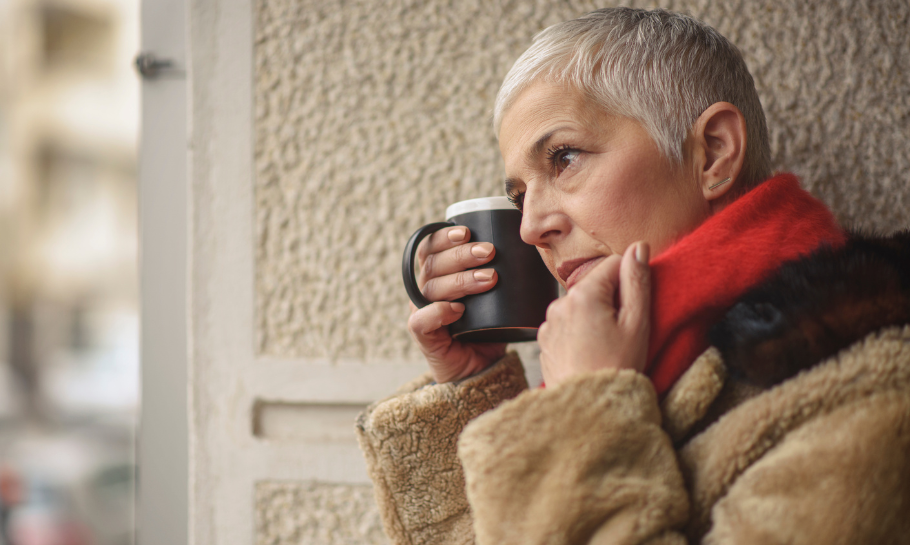 Senior woman holding a coffee mug looking out, very sad. 